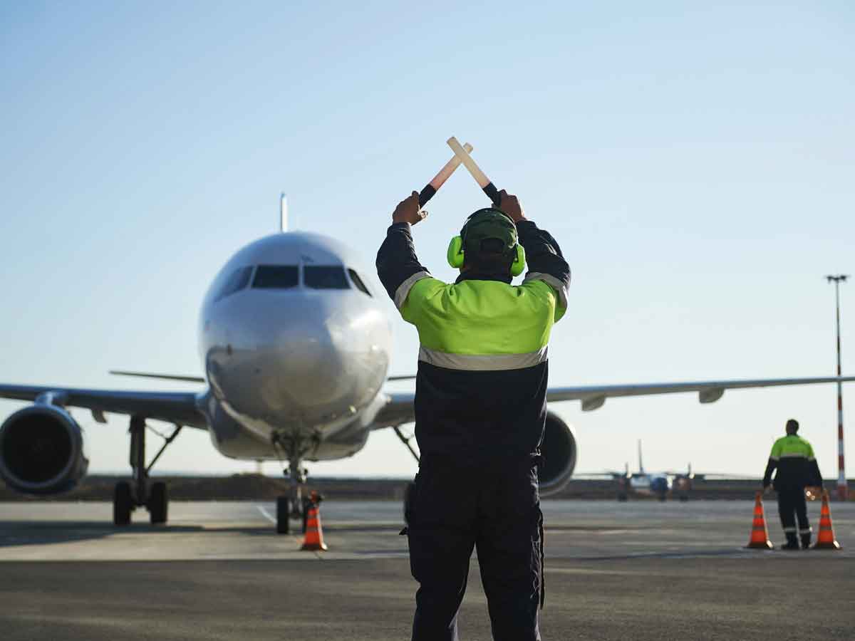 Operario de pista realiza señales frente a un avión comercial