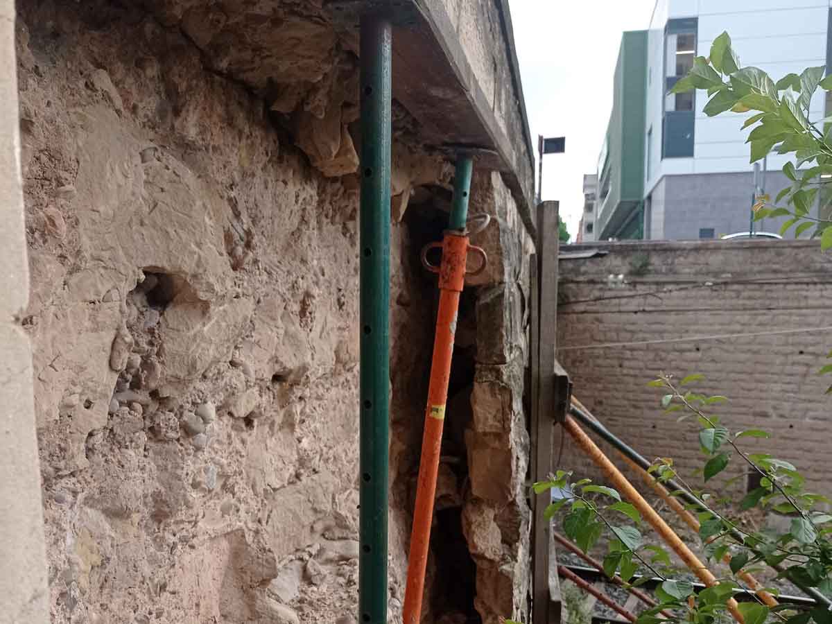 Detalle del muro de piedra deteriorado y sostenido con puntales junto a la vía ferroviaria