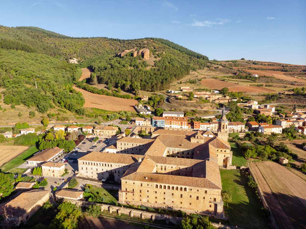 Vista aérea del Monasterio de Yuso en San Millán de la Cogolla, rodeado de montañas y campos de cultivo en la Comarca del Alto Najerilla.
