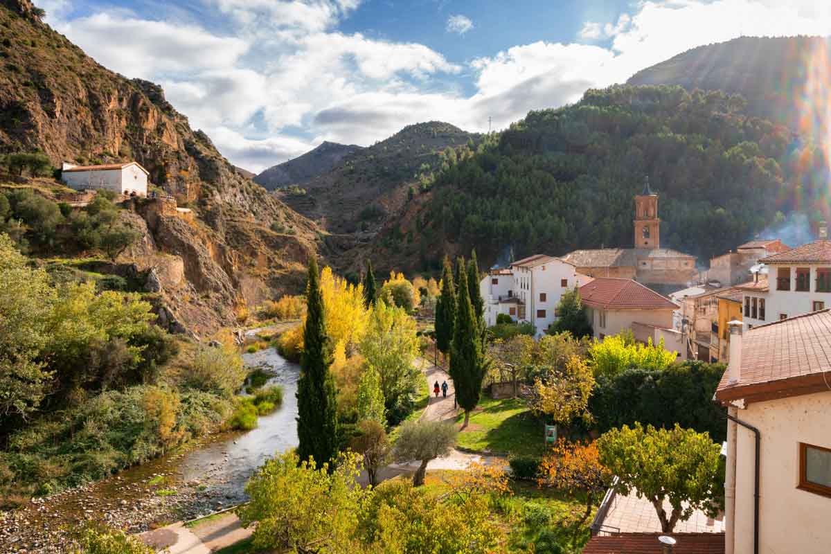 Vista panorámica del río Cidacos a su paso por el municipio de Arnedillo en la Comarca del Alto Cidacos, con árboles otoñales, la torre de la iglesia y montañas escarpadas.