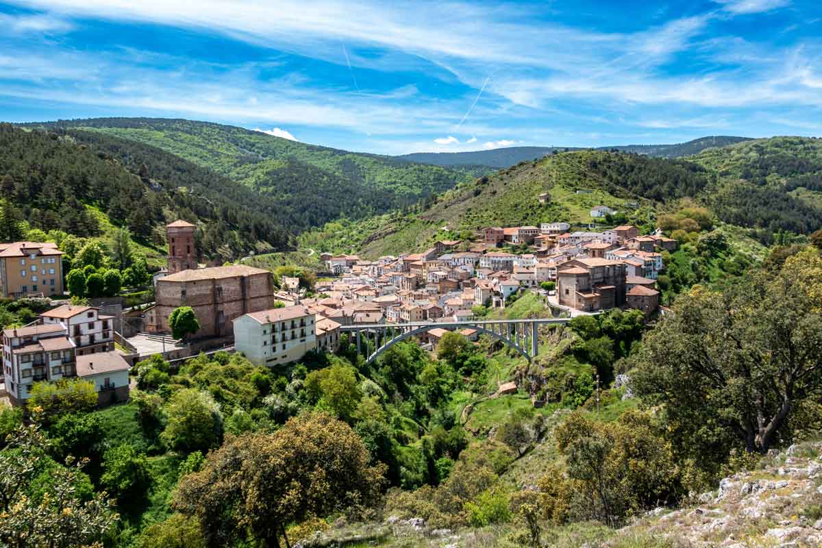 Vista panorámica de Ortigosa de Cameros en la Comarca del Camero Nuevo, mostrando su famoso puente de arco sobre el desfiladero, las iglesias parroquiales y las laderas montañosas cubiertas de pinares.