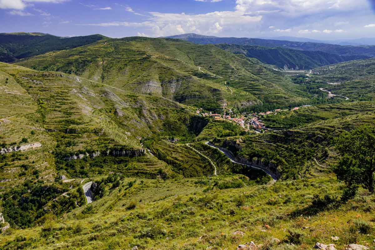 Vista panorámica aérea de la Comarca del Camero Viejo con una carretera serpenteante en el fondo del valle y el pueblo de Trevijano entre laderas montañosas verdes.