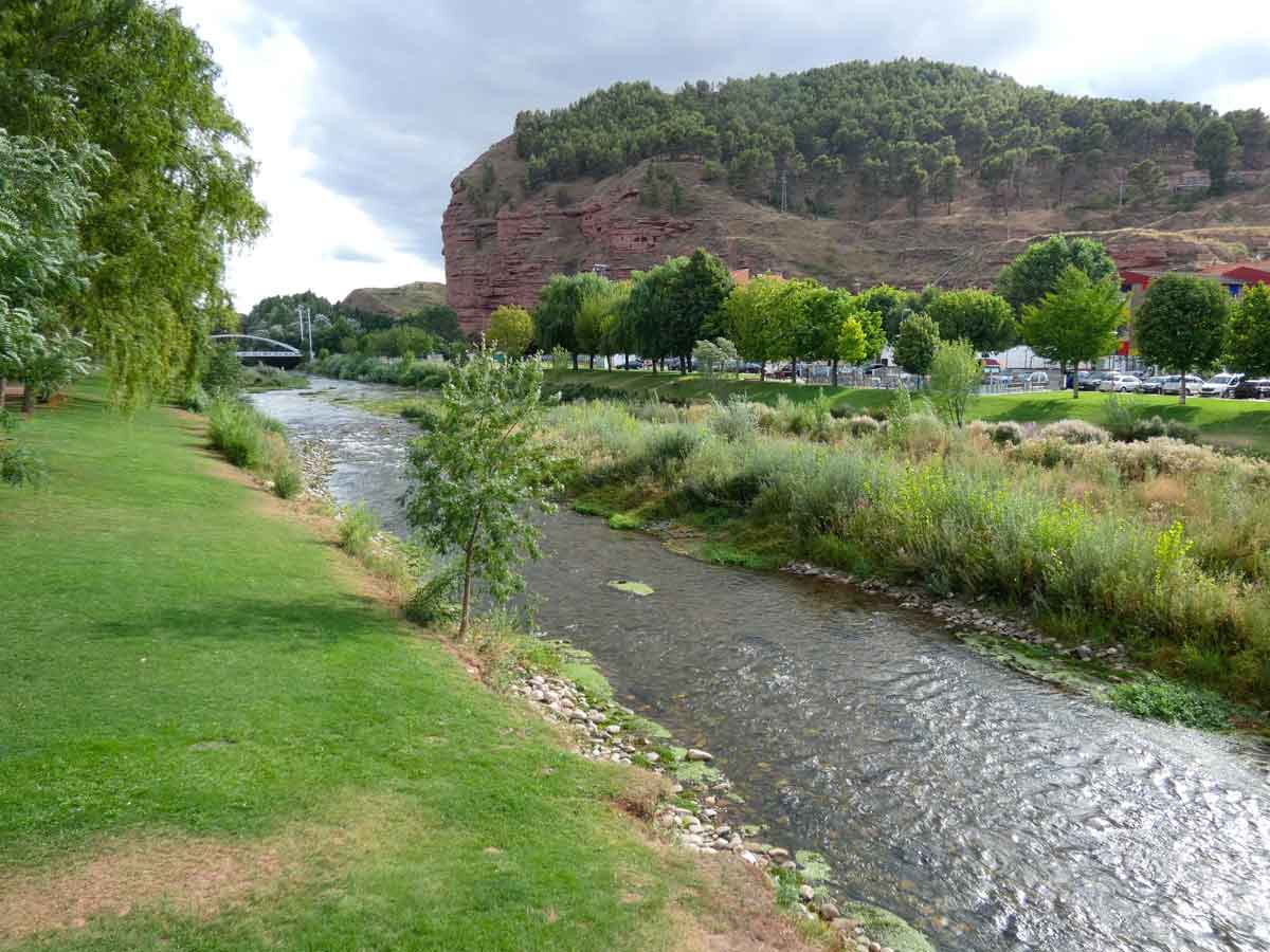 El río Najerilla a su paso por el entorno natural de Nájera, con zonas verdes en la ribera y las características peñas rojizas al fondo.