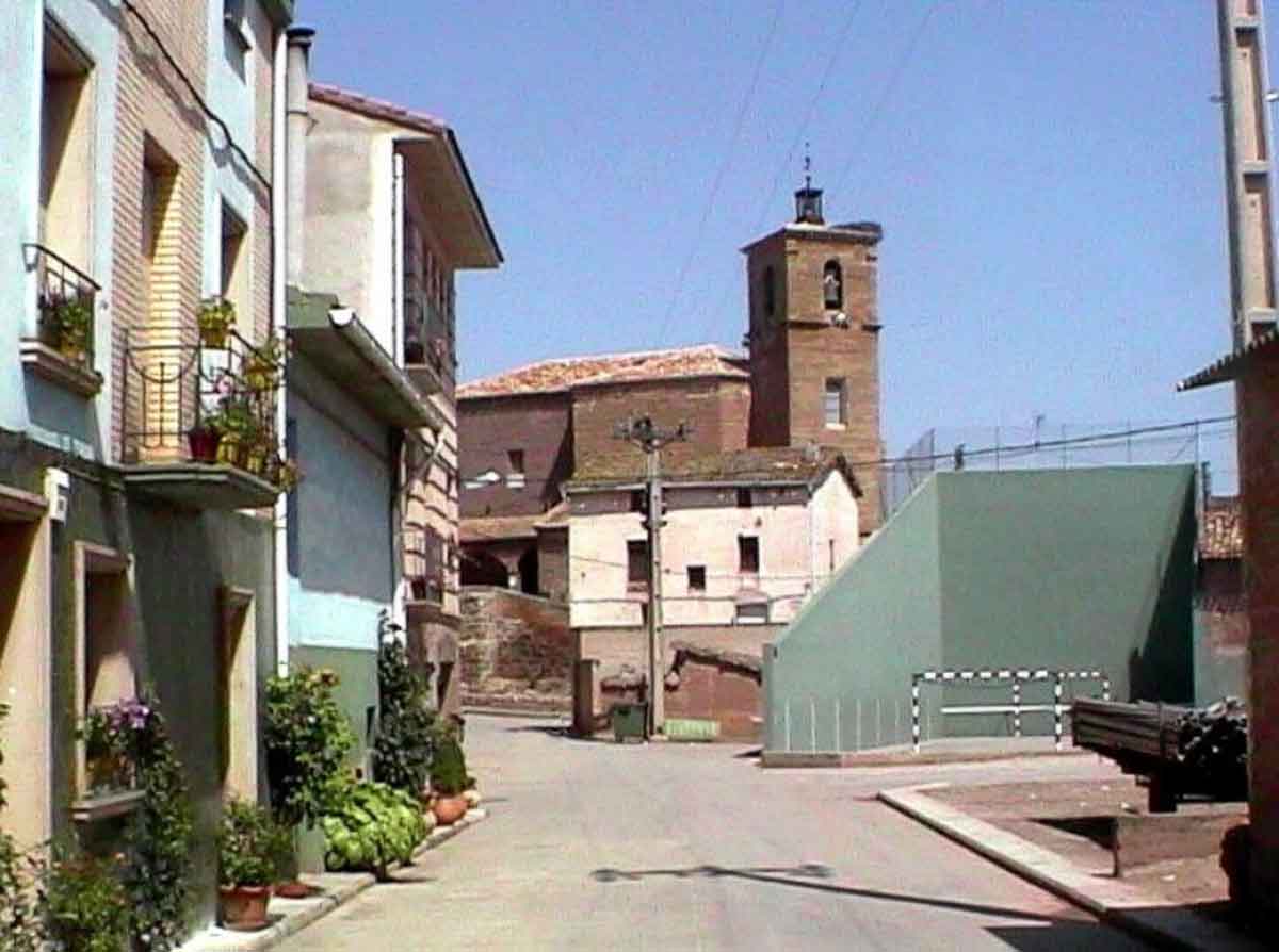 Calle del casco urbano de Azofra con viviendas, frontón y la torre de la iglesia al fondo.