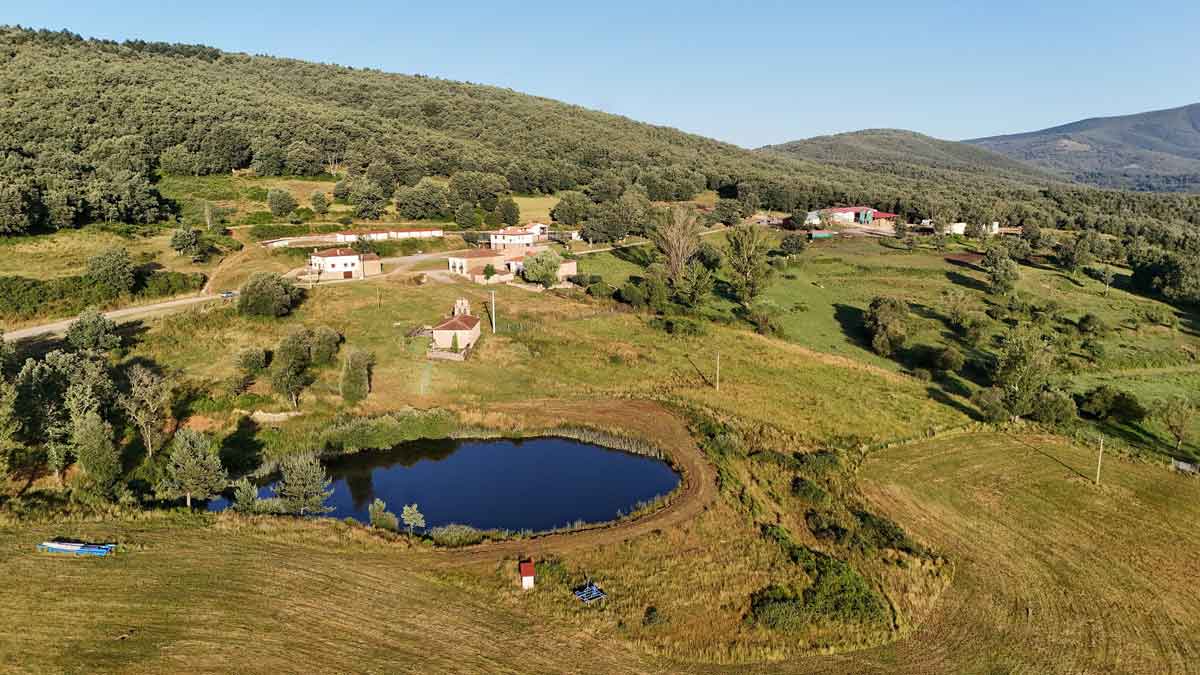 Vista panorámica del entorno rural de Bezares, con una laguna, prados, construcciones dispersas y montes arbolados.