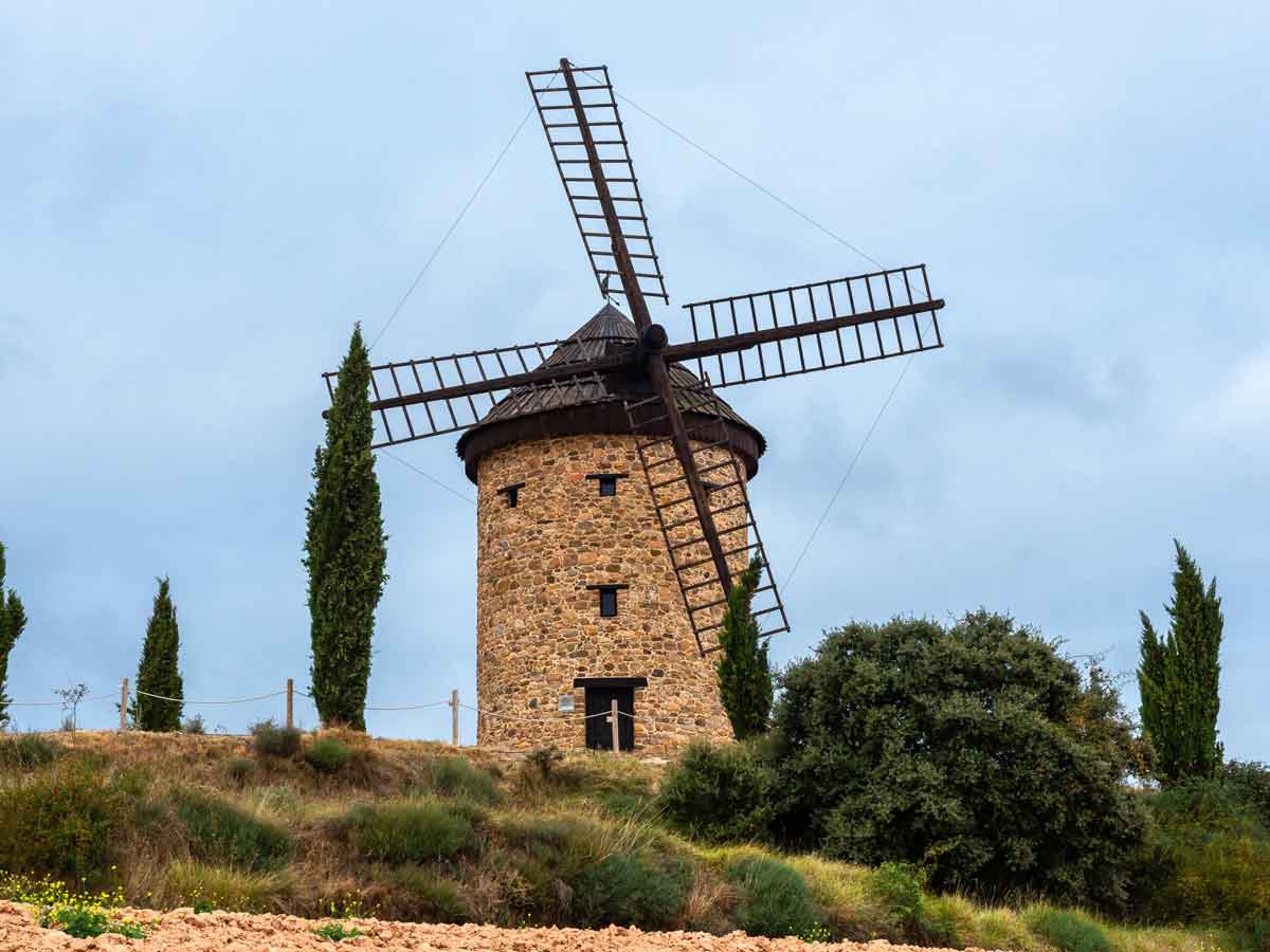 El molino de viento de Ocón construido en piedra con aspas de madera, situado sobre una colina con cipreses bajo un cielo nublado en La Rioja.